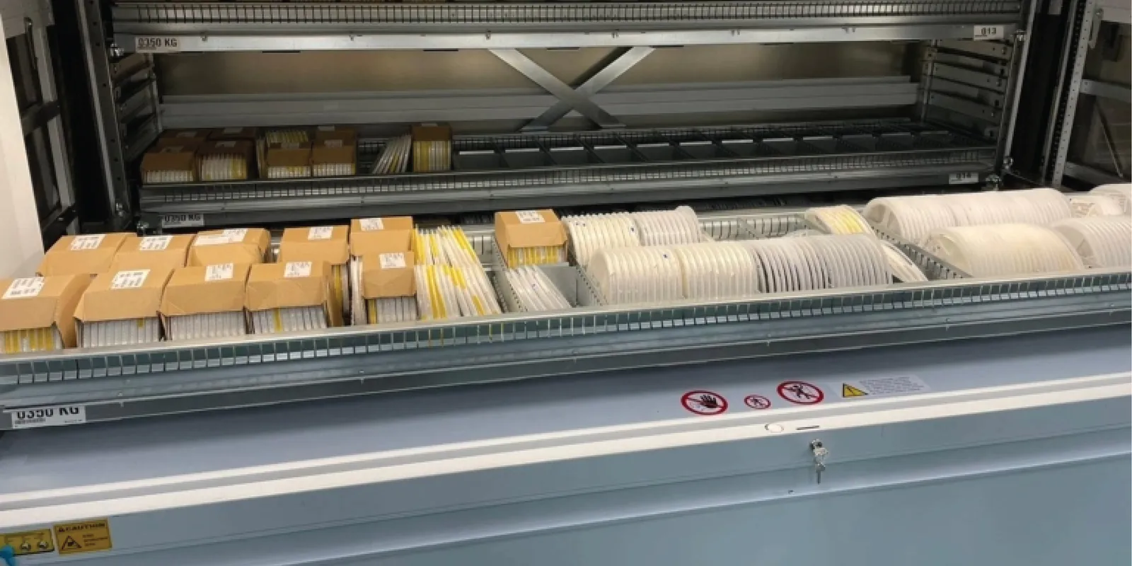 Bahía abierta de un almacén vertical Modula con la bandeja presentada al frente, cargada de cajas y piezas listas para tomar