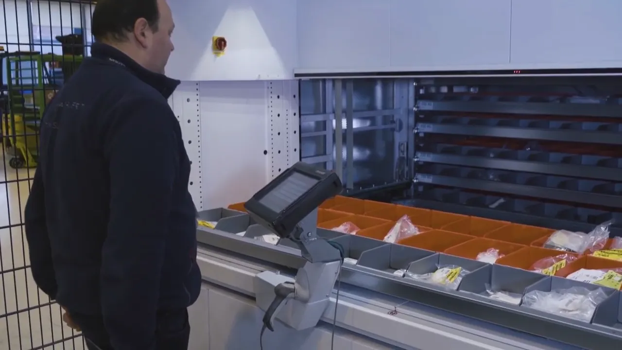 Técnico de Safran frente a la bahía de un almacén vertical Modula con una bandeja de contenedores de componentes; fotografía de la ficha oficial del caso